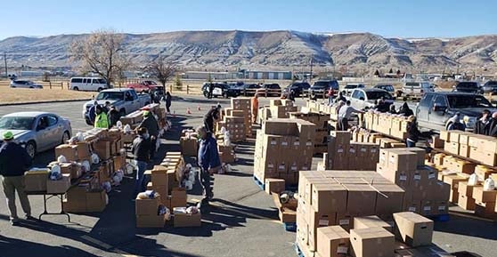 many boxes of food outside with volunteers and mountains in background
