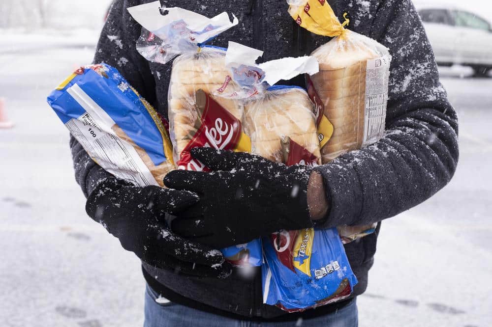 person standing outside in snowy weather holding loaves of bread.