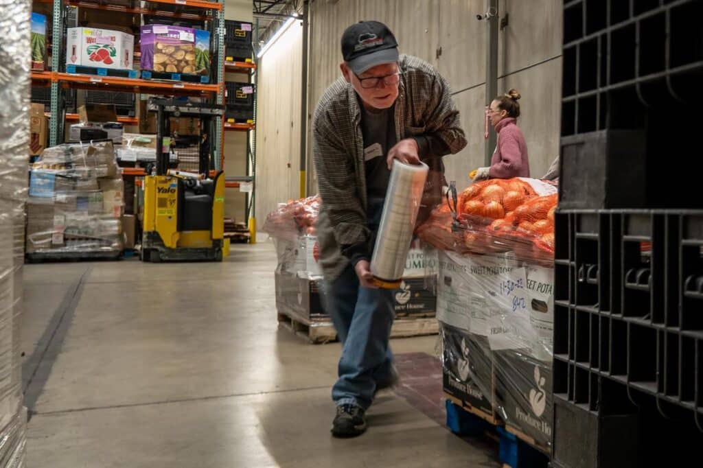 Volunteer wrapping palate of produce in a food bank warehouse