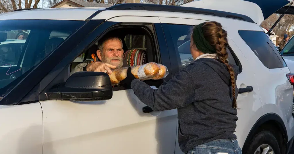 Man being handed bread and other food from a volunteer at a mobile pantry.