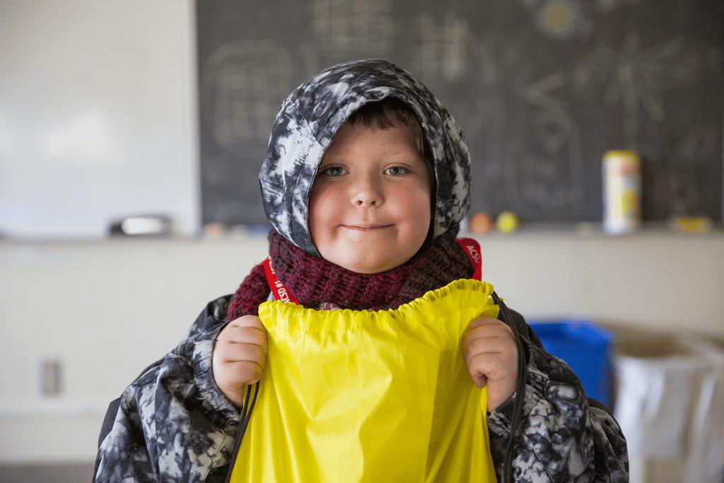 Little boy with a hood on, holding yellow bag.