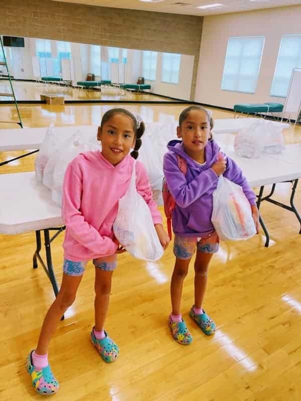 2 girls holding plastic bags filled with food.