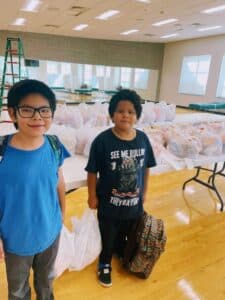2 boys holding plastic bags filled with food.