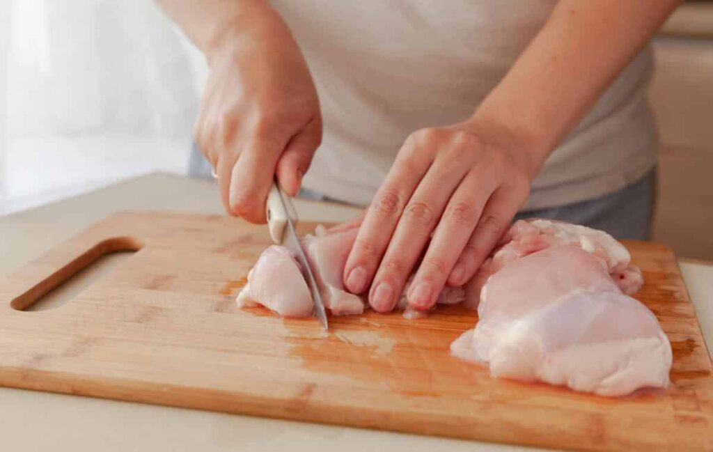 Raw chicken being cut on wooden cutting board.