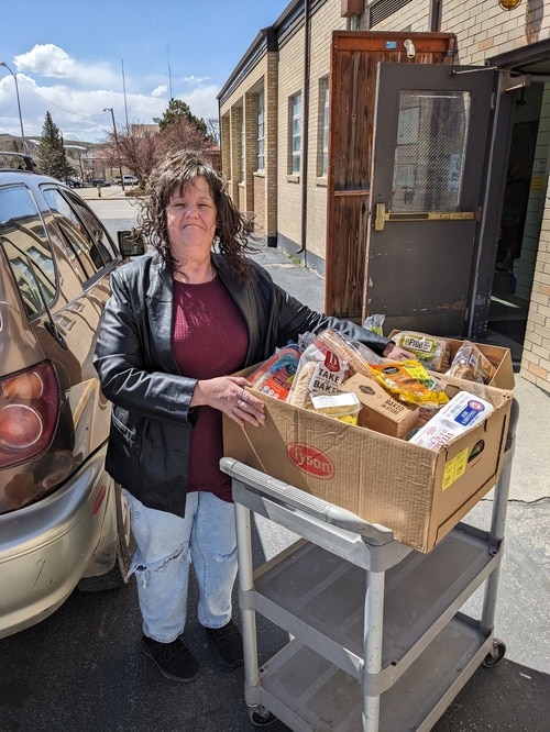 Kandi, a neighbor, stands between her car and a cart with a box of food.