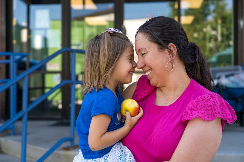 a child holding an apple being held by a woman