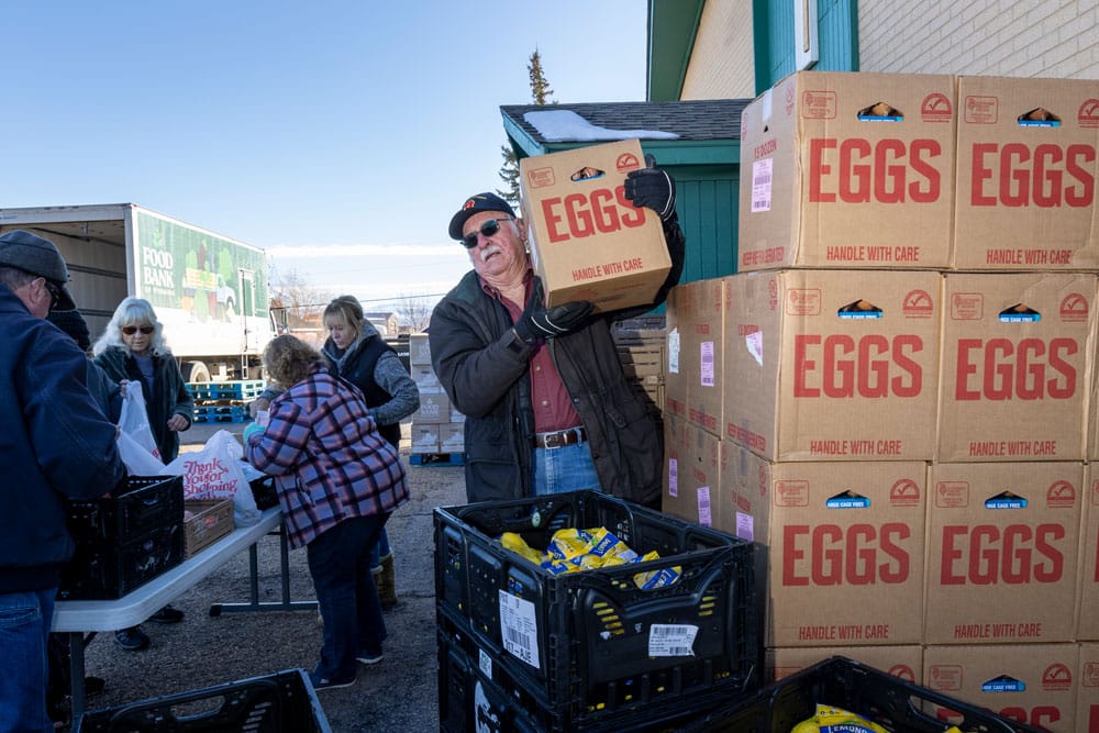 Volunteer carrying a box labled Eggs on his shoulder, pulled from a stack of boxes next to him.