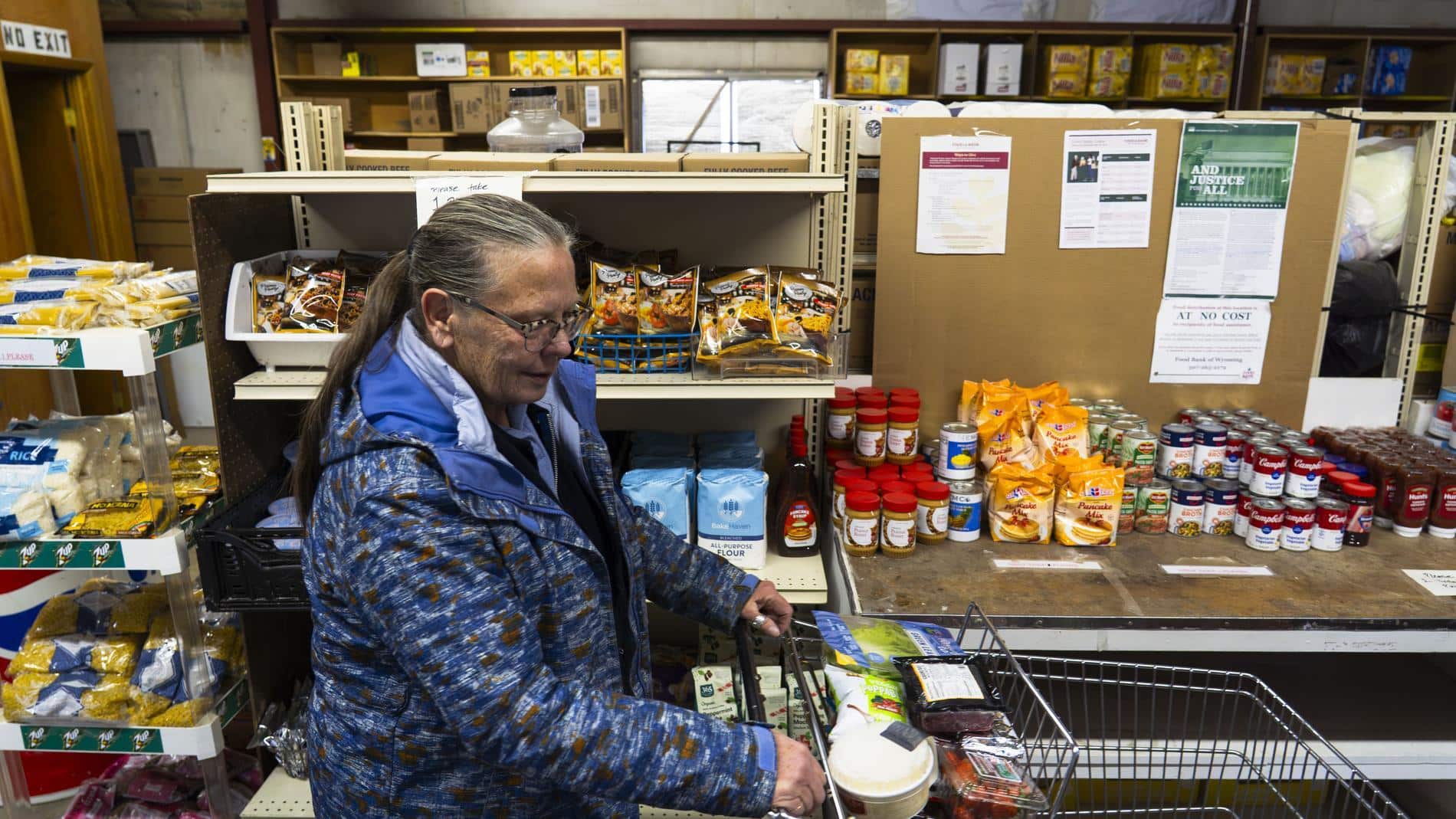 A woman pushes a cart through a food pantry.