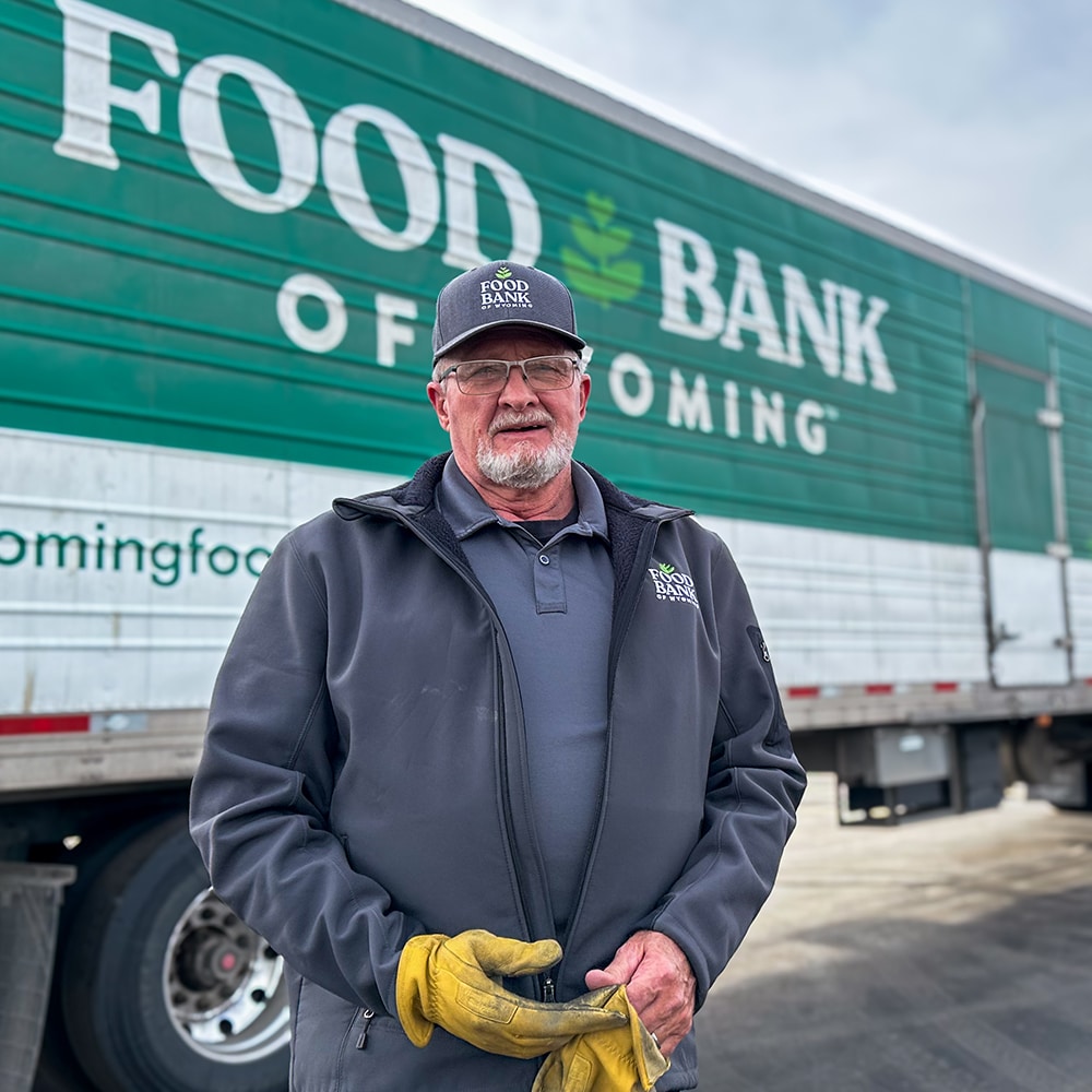 Man standing in front of Food Bank of Wyoming truck looking at camera, one glove on.