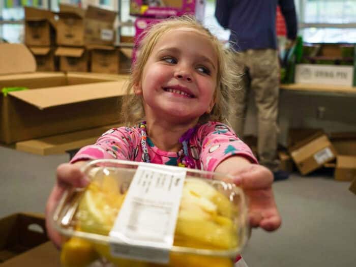 Young girl smiling, holding out a package of cut up pineapples.