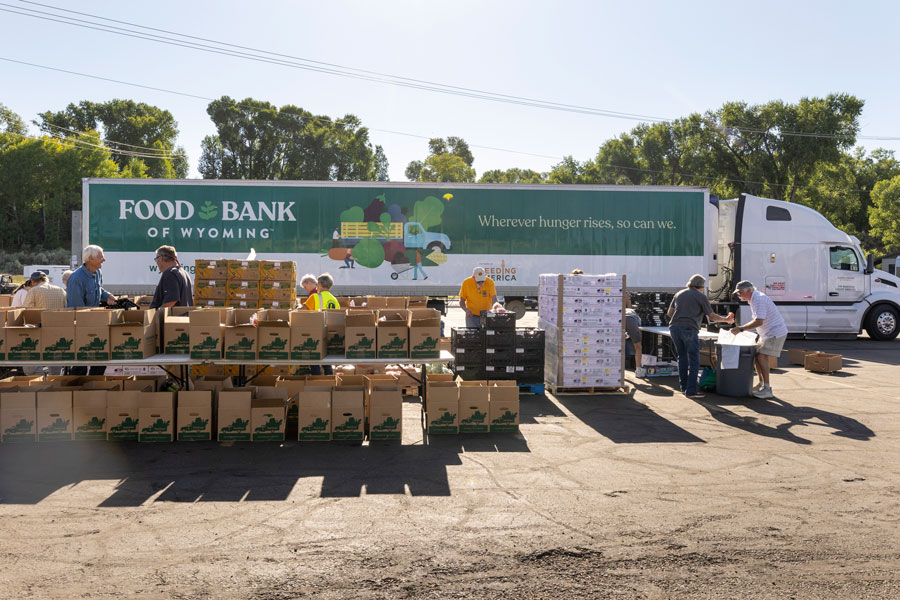 Food distribution wide shot, with food boxes and truck in the background.