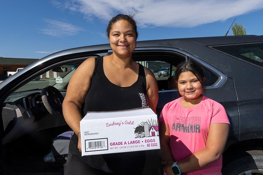 Mom and daughter holding box of eggs in front of their car