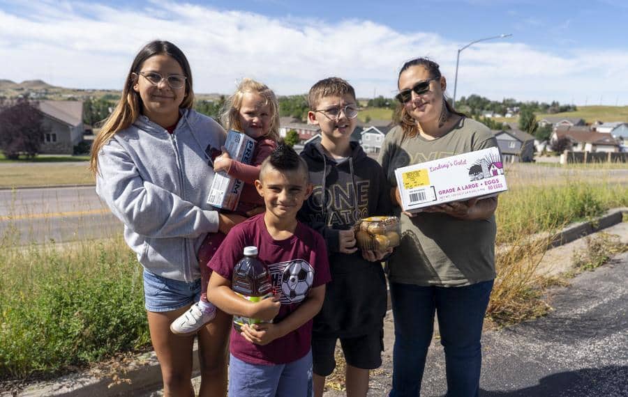 Family of 5 posing outside at a food distribution. Boy in forefront holding a bottle of juice.