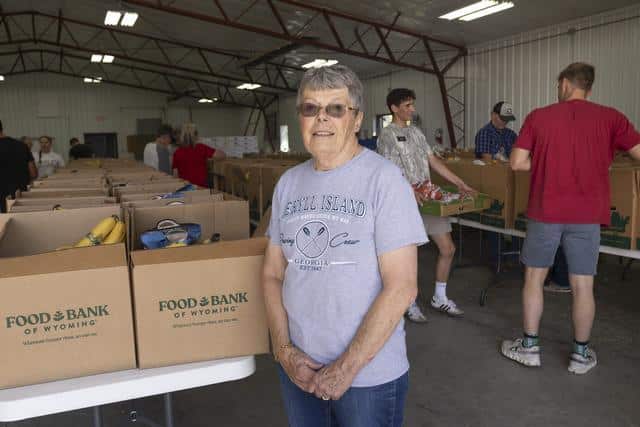 Woman with glasses standing inside a warehouse in front of Food Bank of Wyoming boxes.