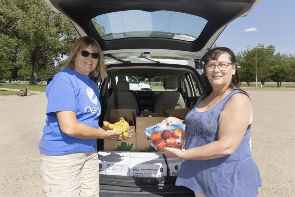 Two women holding produce at the back of a car.