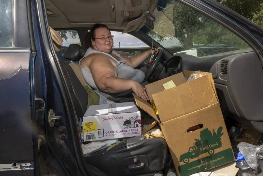 Woman sitting in driver seat of car with food boxes in the passenger seat side.