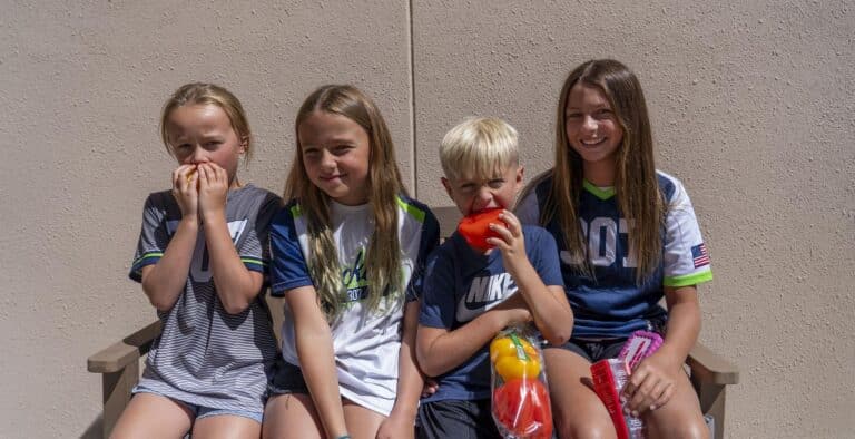 4 children sitting outside, snacking on bell peppers