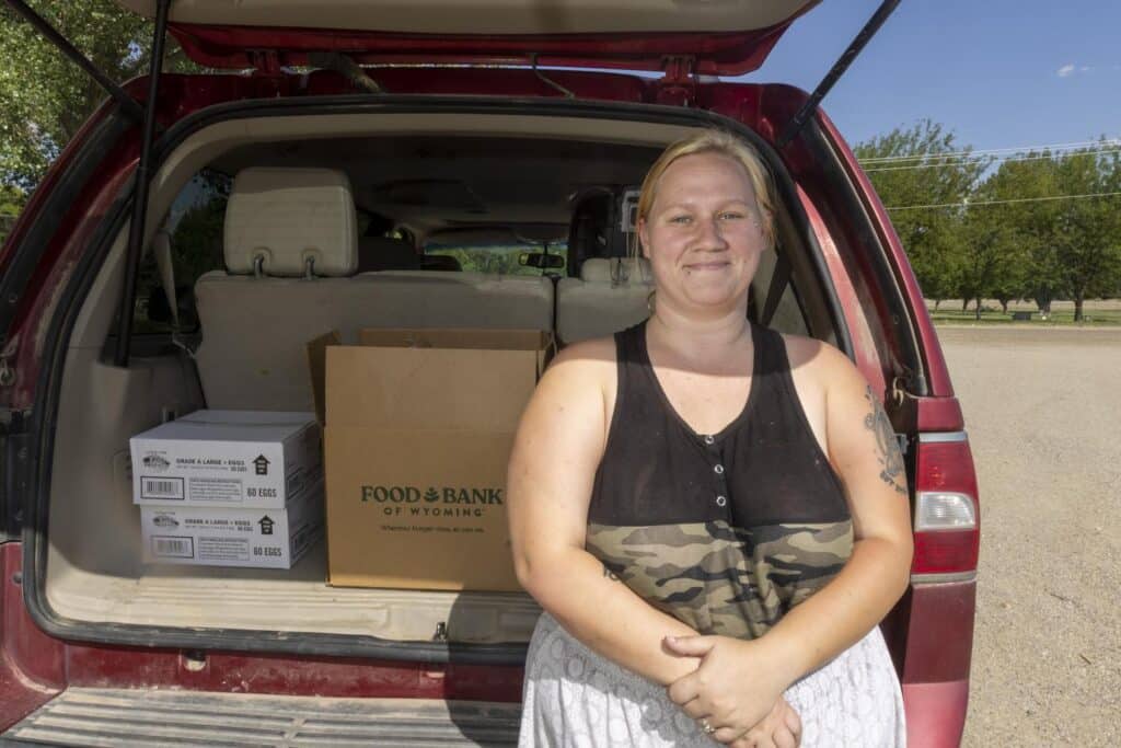Blong woman sitting on the ledge of the back of her car.