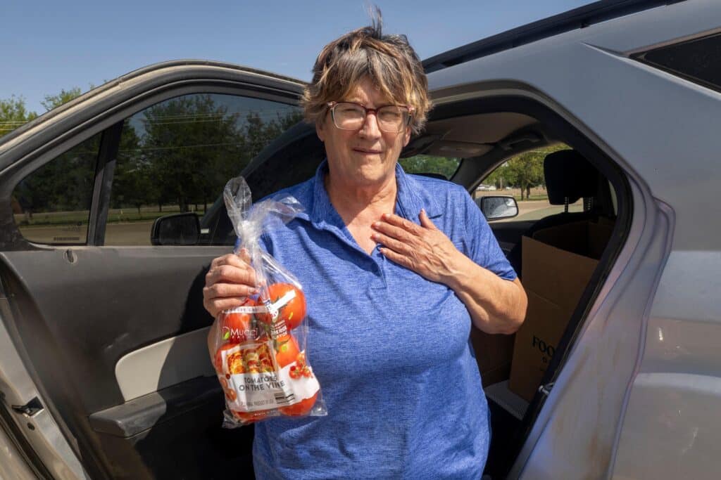 Woman holding bag of tomatoes in front of her car.