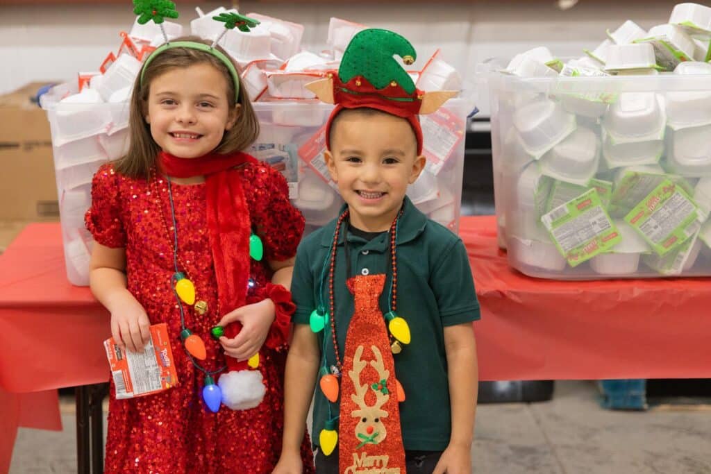 two kids dressed as santa elves, containers of food in the background.