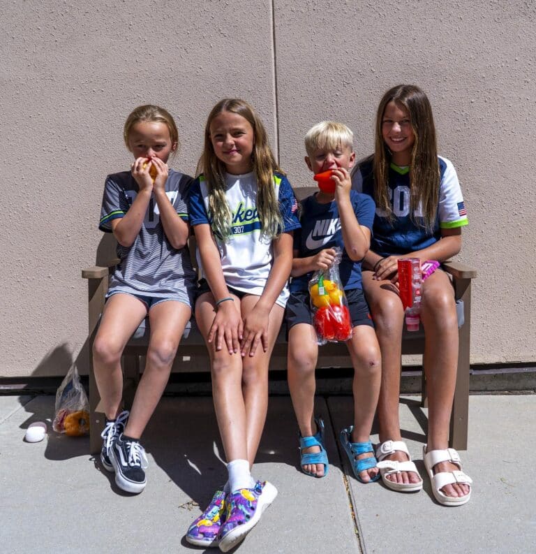 children sitting on a bench outside eating fruit