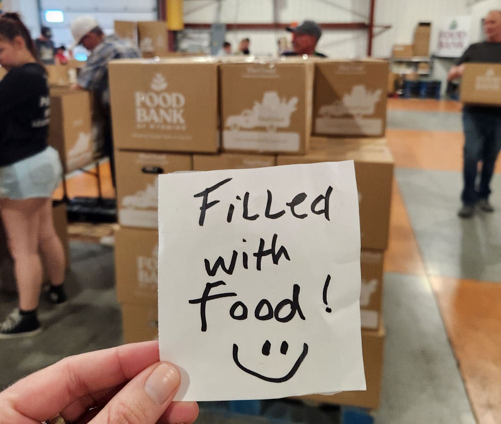 sticky note that says "filled with food" held up in front of a pile of food bank of wyoming food boxes.