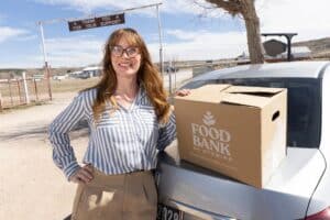 Elaine stands next to car with food box.