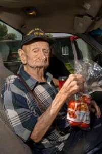 a man in their car holding a bag of tomatoes at a mobile pantry