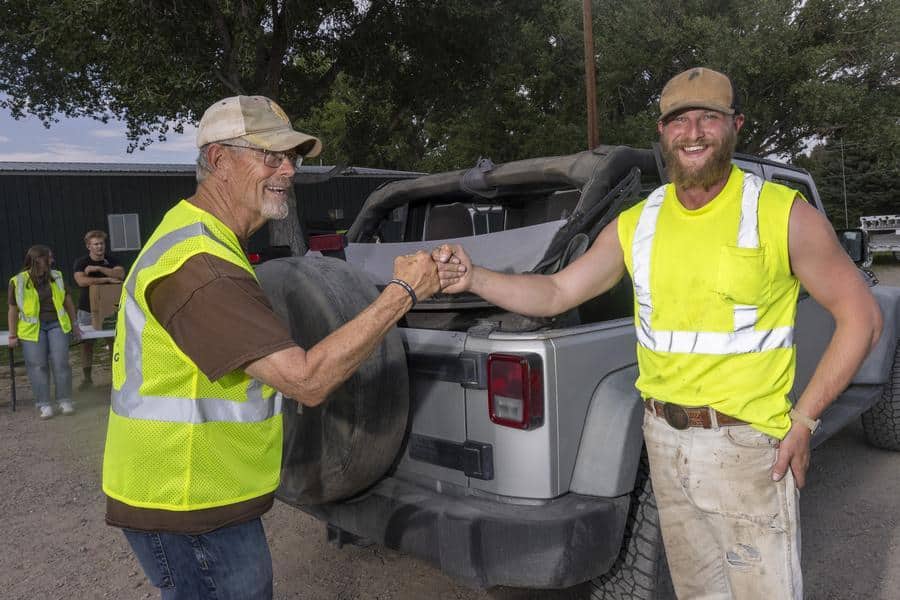 two men fist bumping in front of a truck wearing safety vests.