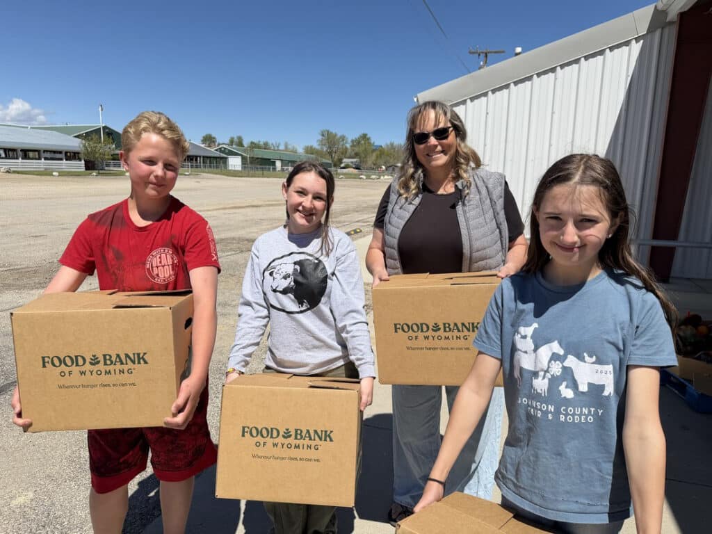 Adult woman and three teens holding Food Bank of Wyoming food boxes.