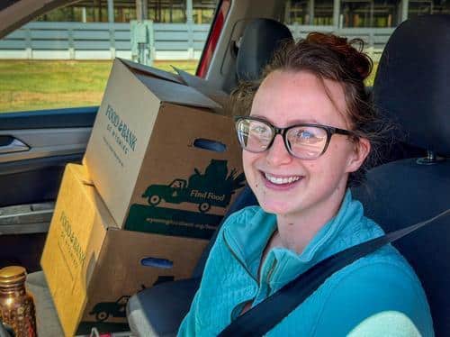 Woman sitting in car with Food Bank of Wyoming boxes in passenger seat.