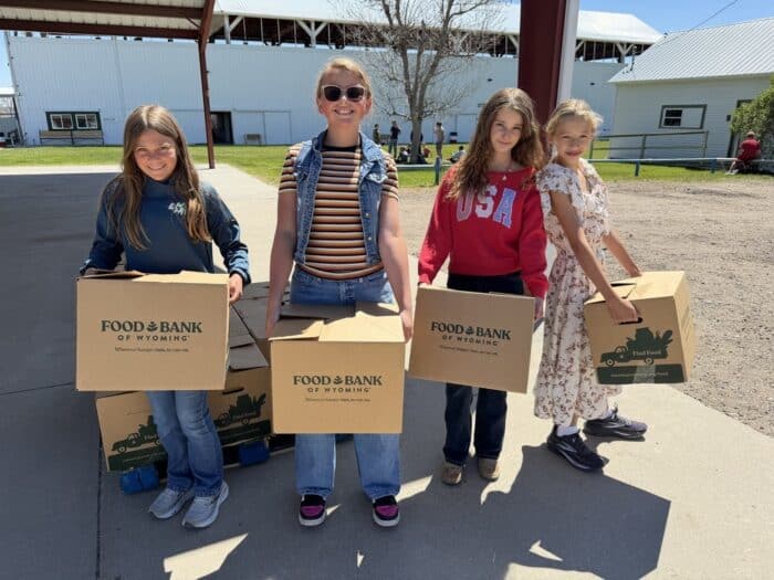 4 kids standing outside holding Food Bank of Wyoming boxes.