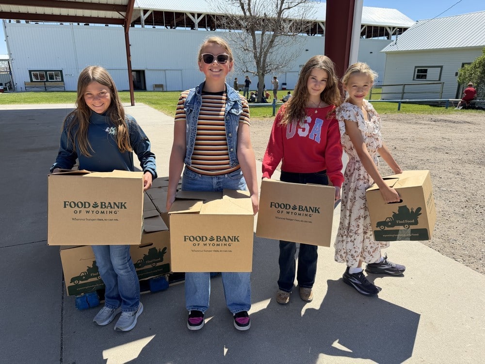 4 kids standing outside holding Food Bank of Wyoming boxes.
