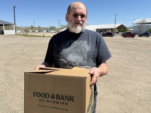 Michael, a mobile pantry attendee, poses holding a Food Bank of Wyoming food box outside.