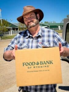 Phil, a mobile pantry attendee, posing, holding a Food Bank of Wyoming box outdoors.