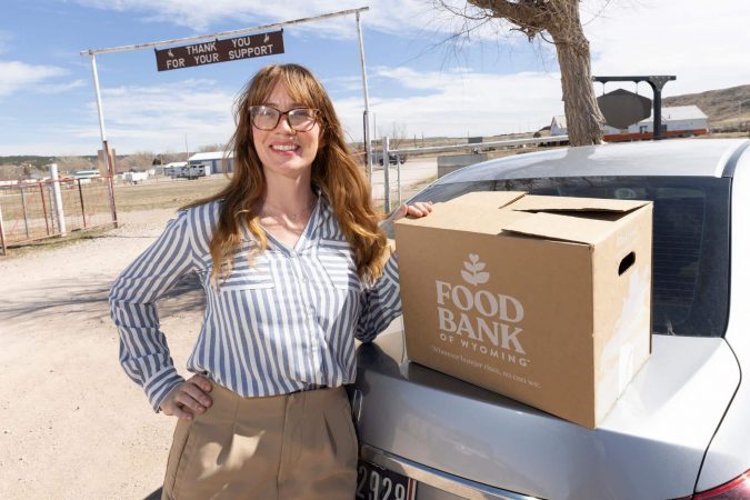 Elaine stands next to car with food box.